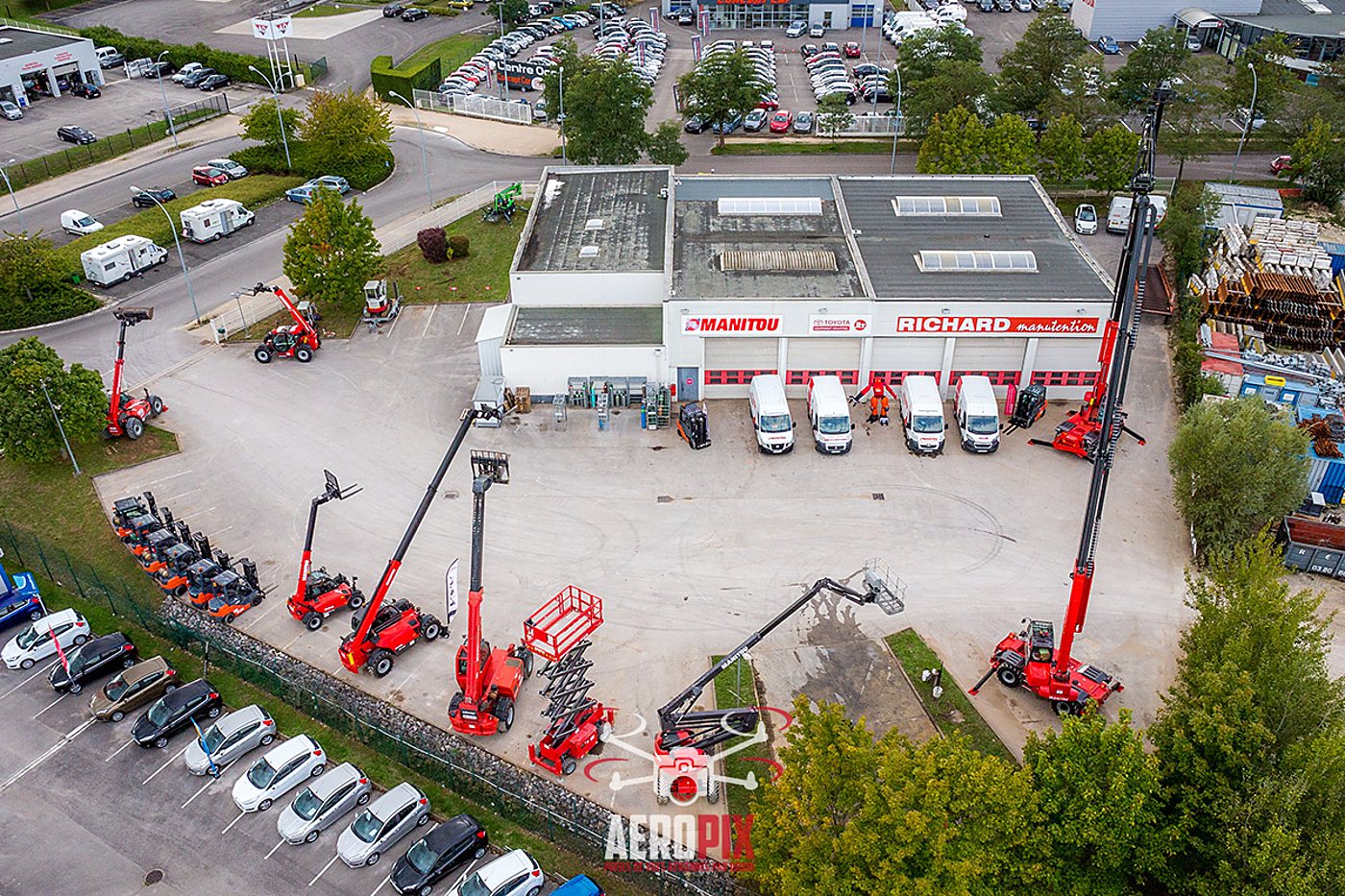 Vue aérienne d'un bâtiment Richard manutention entouré de chariots télescopiques, nacelles et fourgons blancs garés sur le parking.