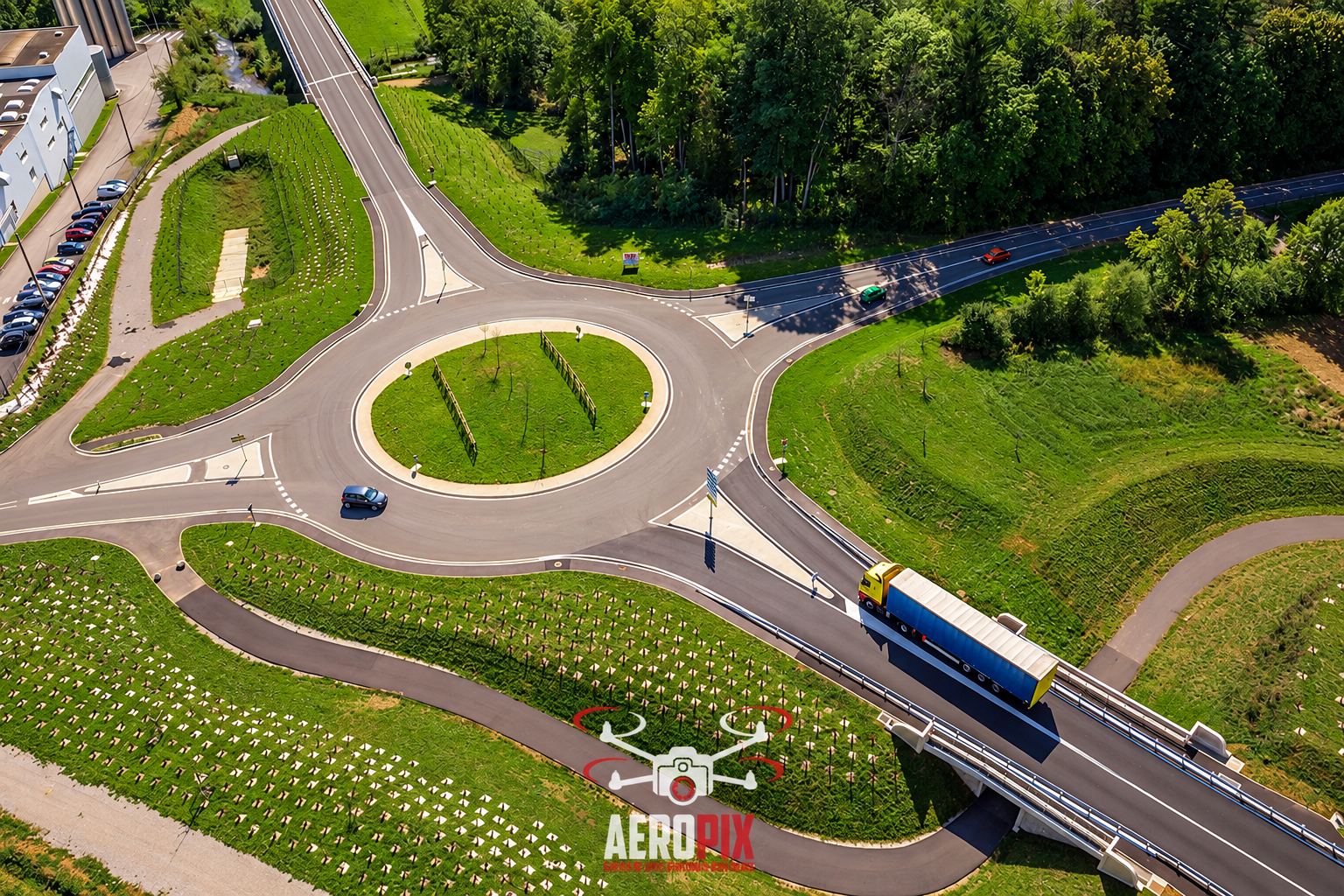 Photo prise par drone d'un rond-point entouré de talus herbeux, avec un camion bleu et jaune qui roule sur un pont routier.